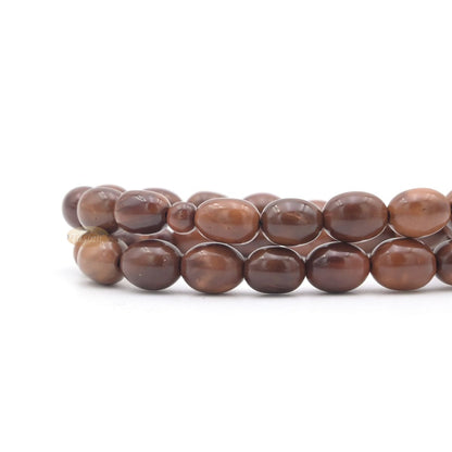 Brown wooden Islamic misbaha prayer beads with elongated oval beads and green tassels.